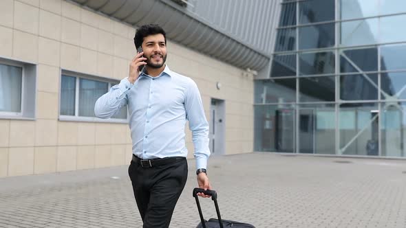 Business Trip. Handsome Man With Phone And Suitcase At Airport