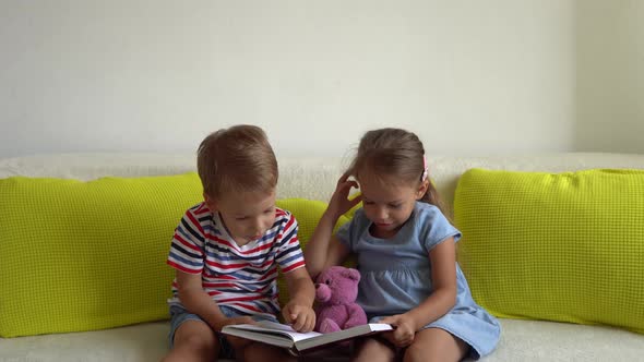 Two Cute Preshool Toddler Children Read Book of Fairy Tales On Couch