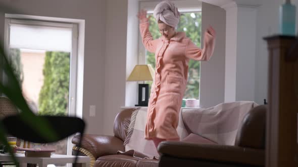 Wide Shot Joyful Millennial Woman Jumping on Couch in Living Room at Home in Slow Motion