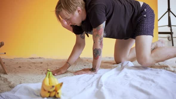 Young Handsome Blond Man Preparing Background Sand Beach Decorations for Shooting in Studio