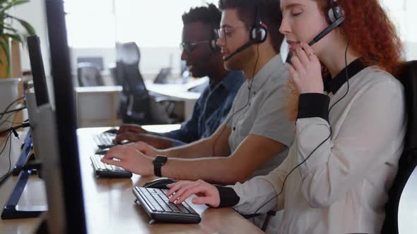 Side view of young cool mixed-race call center team calling and sitting at desk of modern office 4k