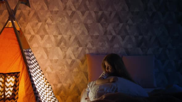 Offended Child with Pillow Looks at Play House with Lamp