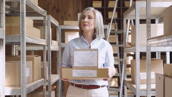 Confident Mature Woman Holding Parcel Boxes Walking in Warehouse