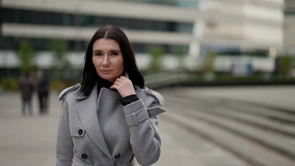 a Brunette in a Gray Coat Walks Through a Modern Urban Area