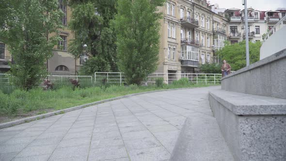 Wide Shot of Cheerful Young Caucasian Girl Riding Scooter Outdoors. Portrait of Happy Smiling