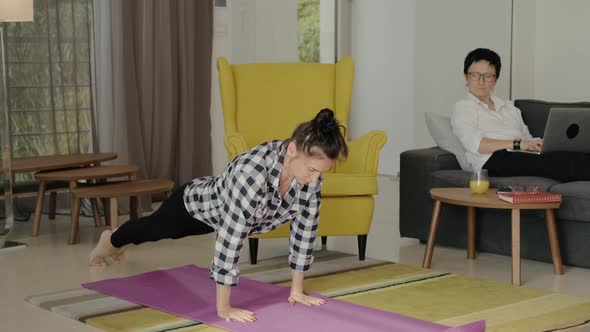 Young Woman is Doing Plank Exercise Her Friend Working with Laptop on Sofa at Home Room Rbbro