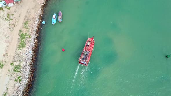 Red Fishing Boat Sails Along the Coast in Turquoise Sea, Aerial View.