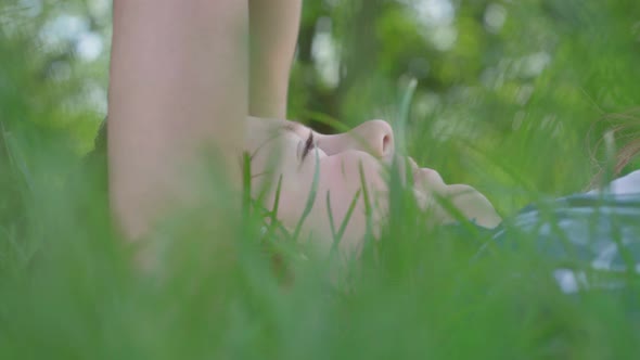 Close Up Portrait of Little Girl Kissing Forehead of the Boy Lying in the Grass. A Couple of Happy