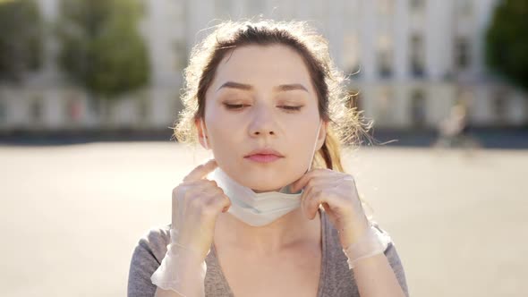 Beautiful Young Woman with a Medicinal Mask on Face Use Phone Walking at Sunlight on Street