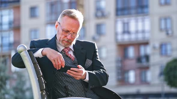 Mature Businessman with Beard and Glasses Sitting on Bench in the City