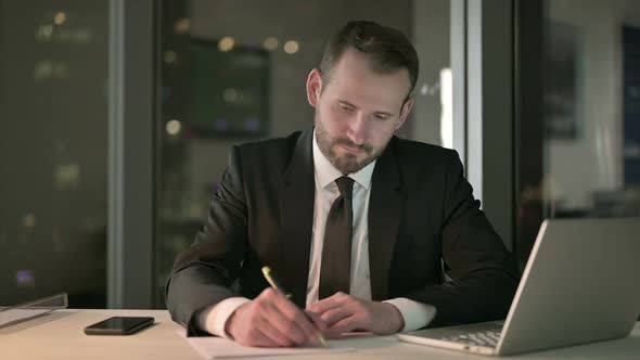 Young Businessman Writing Document on Office Desk at Night