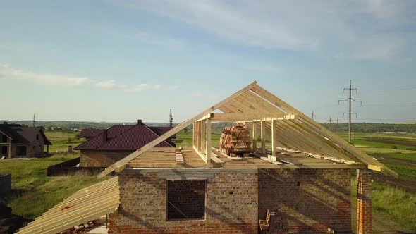 Aerial view of unfinished brick house with wooden roof frame structure under construction.