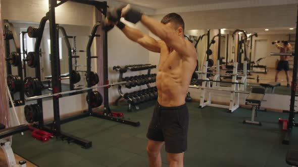 Young Muscular Man Working Out in the Gym and Doing Straight Arm Swings with Dumbbells to Work Out