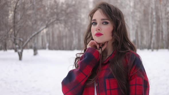 Young Woman with Wavy Hair Standing and Touching Face in Winter Forest