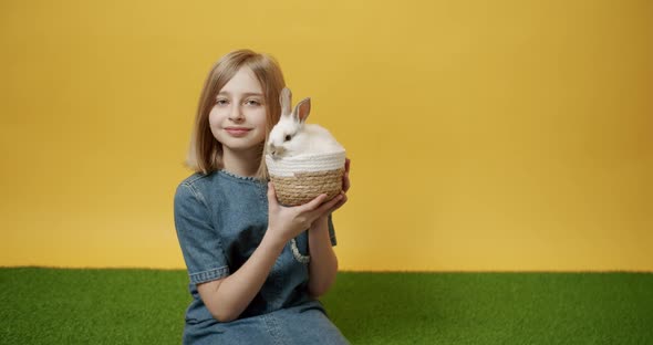 Teenager in a Blue Dress Holds a Basket with a Rabbit in Her Hand and Kisses It