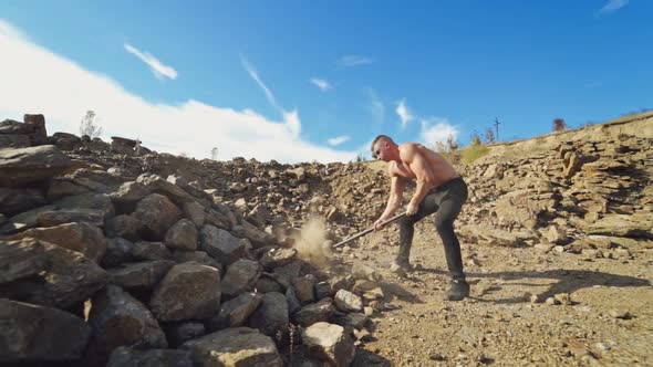 Sportsman with hard hammer on the rocky background. Athletic man without shirt breaking stones with 