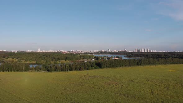 Aerial View of Green Field and Blue Hand Riverbed Surrounded By Trees Near City