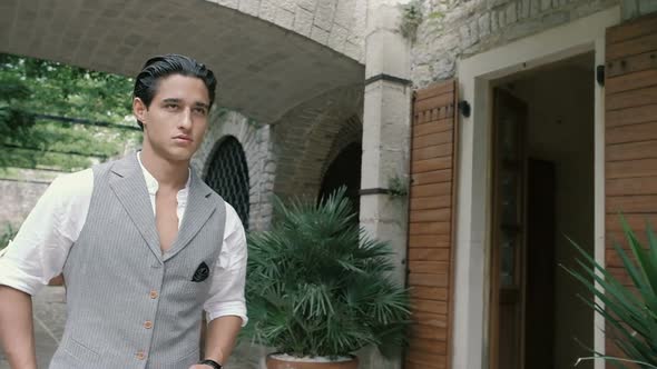 Attractive young man in a suit walks around the old town along the plants. Slow motion