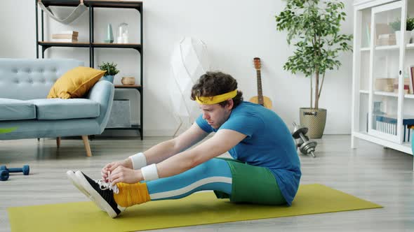 Awkward Guy in Bright Sports Outfit Stretching Body Then Tying Shoelaces Exercising on Yoga Mat at