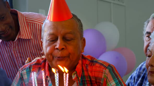 Senior man blowing out the candles on a birthday cake with his friends 4k