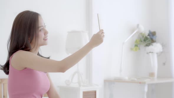 Beautiful young asian woman sitting taking a selfie with smart phone on bedroom.