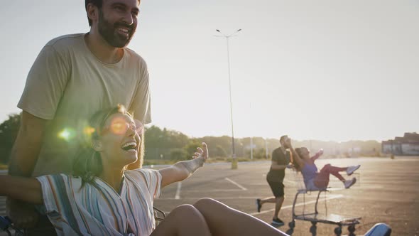 Young Guys and Girls Riding on Shopping Carts at Empty Car Parking