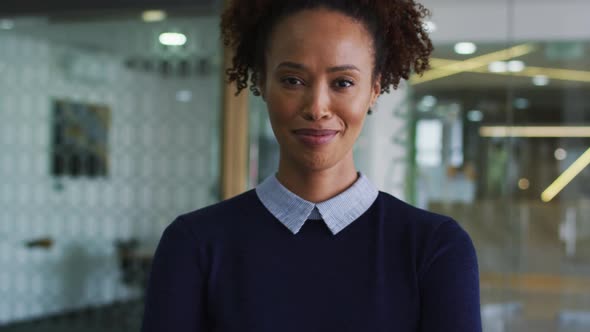 Portrait of smiling mixed race businesswoman in blue jumper standing in office