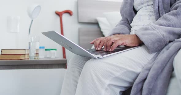 Mid section of african american senior woman using laptop while sitting on the bed at home