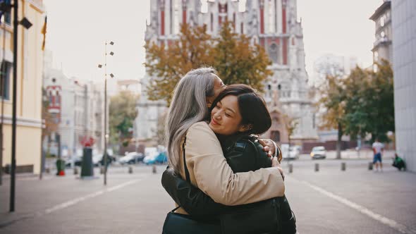 Asian Mature Mother and Adult Daughter in Casual Outerwear are Meeting at a City Square Smiling