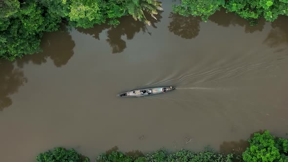 Aerial top down shot of boat cruising over amazon river in South America during cloudy day