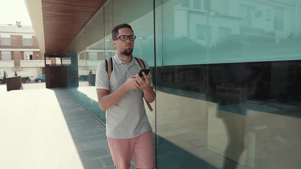 Alone Male Tourist Is Walking on Street, Looking on Screen of Smartphone