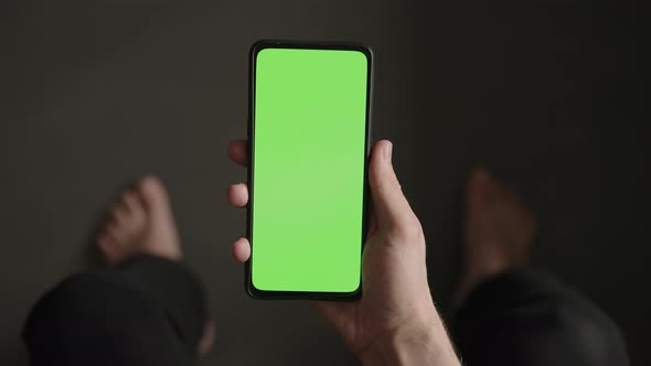 POV Top View Shot of Man Show Phone with Green Screen Indoor Sitting on a Couch