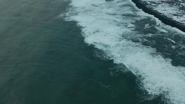 Rotating drone shot of waves crashing on black sand beach in Iceland.