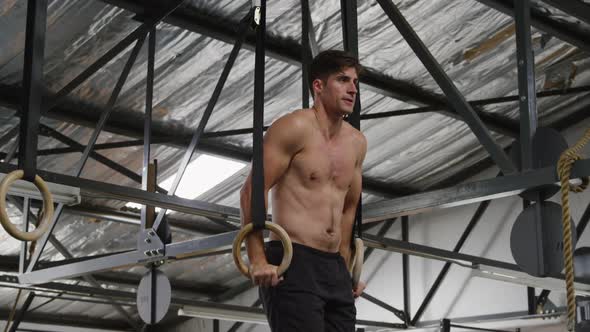 Side view athletic Caucasian man lifting on gymnastic rings