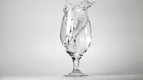 Super Slow Motion Ice Falls Into a Glass of Water with Spray