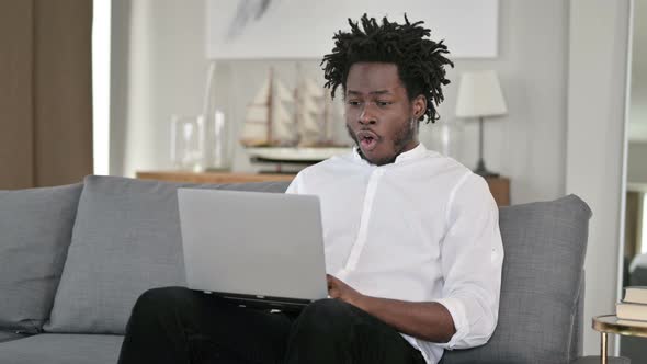 African Man Celebrating Success on Laptop at Home 