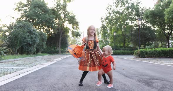 Cute Little Caucasian Kids with Blonde Hair Seven Years Old in Costume of Witch with Hat and Baby