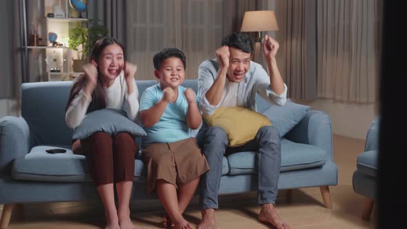 Asian Family Celebrating While Watching Tv Together Sitting On A Sofa In The Living Room At Home