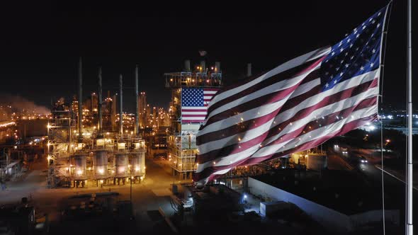 American Flag in Front of the View of Large Petroleum Refinery Working at Night Time alt
