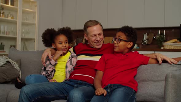 Happy Grandpa with Adorable School Age Multiracial Kids Bonding on Sofa at Home