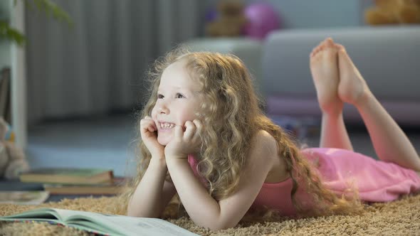 Cute Curly-Haired Girl Lying on Soft Carpet at Home and Smiling, Happy Child