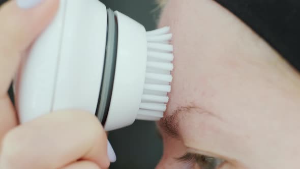 Young woman cleaning face using cosmetic face brush. Facial. Cosmetic procedures.