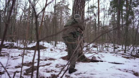 Back View Cautious Soldier Walking to Tree Trunk Aiming with Weapon Outdoors