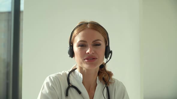 Professional Female Doctor in White Medical Coat and Headset Making Conference Call on Laptop