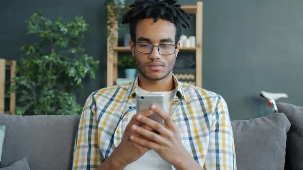 Happy African American Student Using Smartphone at Home Relaxing on Sofa Alone