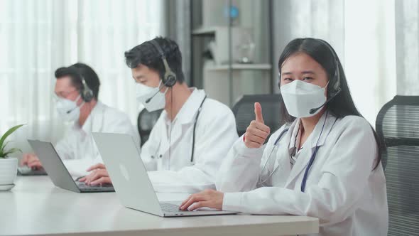 A Woman Of Three Asian Doctors In Mask Working As Call Centre Agent Looking At Camera And Thumbs Up