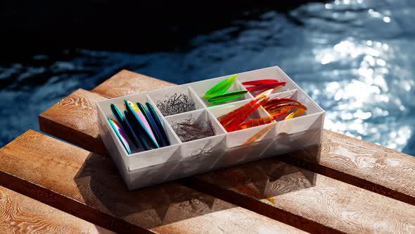 Fishing accessories in a box on a wooden pier. Colourful fish-baits and tools.