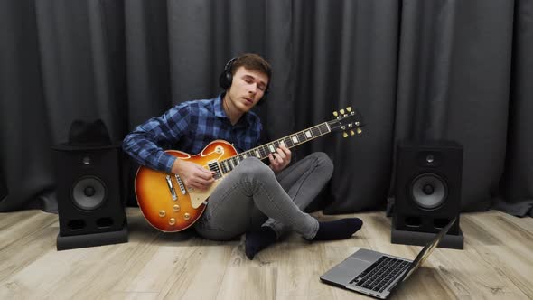 Man playing on electric guitar with headphones on rehearsing a song at home music recording studio