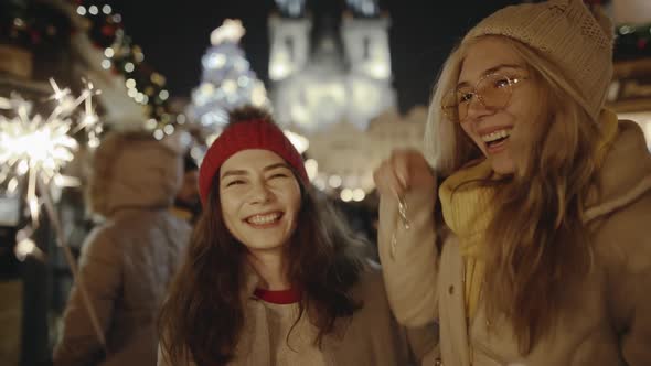 Adorable Young Girlfriends Laughing and Hugging at Festive Cozy Fair in the Central Square of Prague