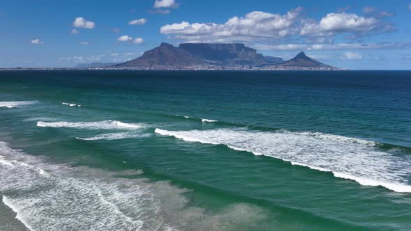 Flight above azure blue waves on Cape town beach toward Table mountain; drone